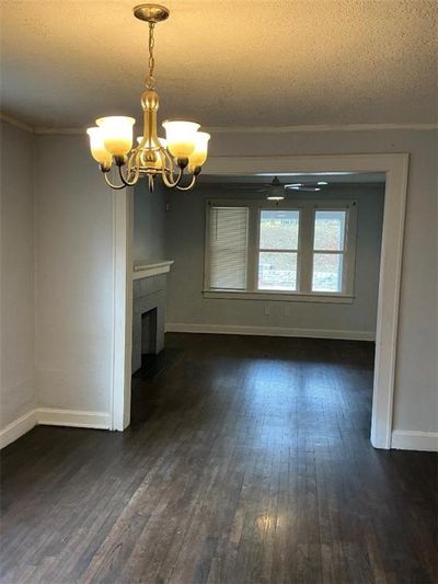 Unfurnished living room featuring dark hardwood / wood-style flooring, an inviting chandelier, a textured ceiling, and ornamental molding | Image 3