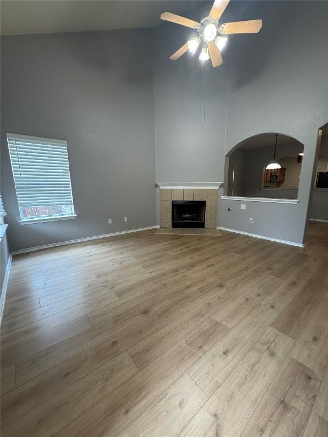 Unfurnished living room featuring a ceiling fan, wood finished floors, a towering ceiling, a fireplace, and baseboards | Image 13