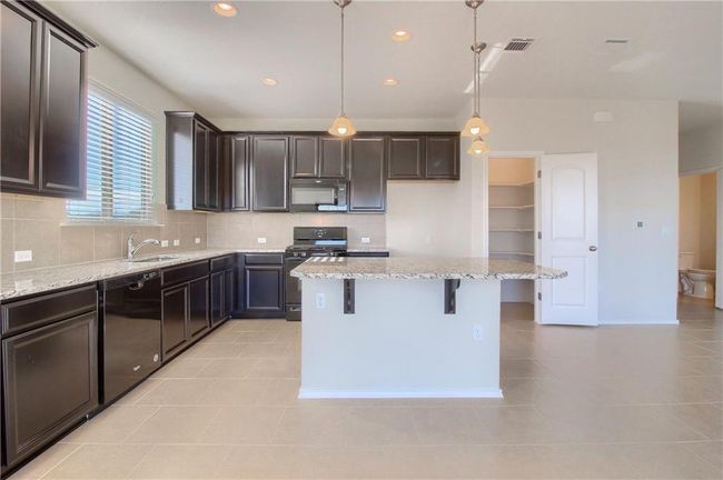 Kitchen with black appliances, light tile patterned floors, decorative backsplash, light stone counters, and dark brown cabinets | Image 6