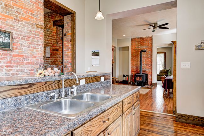 kitchen featuring dark wood-style floors, a ceiling fan, a wood stove, decorative light fixtures, and a sink | Image 24