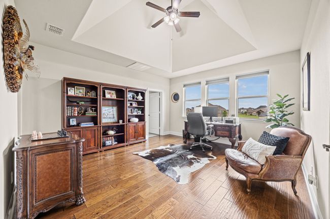 Office space with a tray ceiling, ceiling fan, wood floors, and baseboards | Image 12