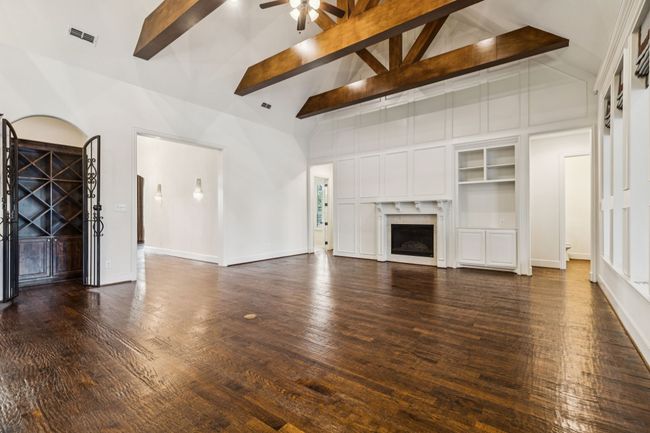 Unfurnished family room featuring ceiling fan, beamed ceiling, high vaulted ceiling, dark wood-style floors, wine cellar, and a fireplace | Image 14