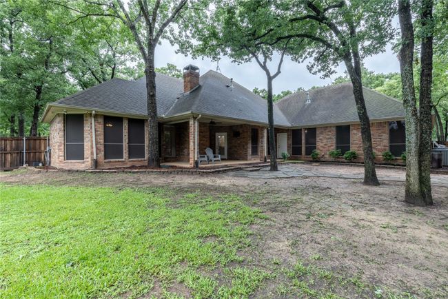 Rear view of house with a patio, a shingled roof, a chimney, and brick siding | Image 10