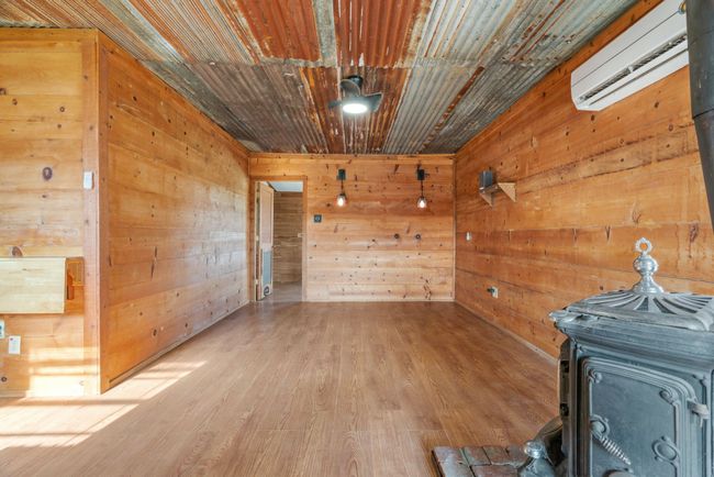 Empty room featuring a wall mounted air conditioner, a wood stove, wooden walls, and wood finished floors | Image 29