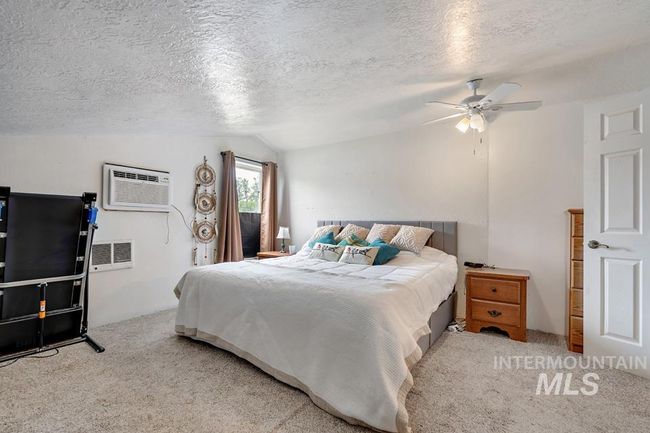 Carpeted bedroom featuring lofted ceiling, a wall unit AC, a ceiling fan, and a textured ceiling | Image 21