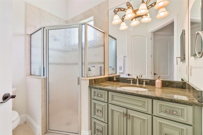 A charming guest bath that doesn’t skimp on style—featuring a custom vanity with elegant detailing, rich stone countertops, and a private walk-in shower bathed in natural light. | Image 22