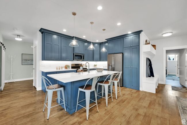 Kitchen with appliances with stainless steel finishes, blue cabinetry, light countertops, a kitchen breakfast bar, and light wood-type flooring | Image 12