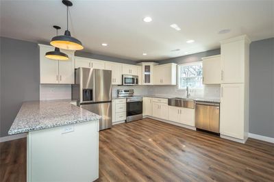 Kitchen with white cabinetry, stainless steel appliances, hanging light fixtures, kitchen peninsula and kitchen pantry | Image 1