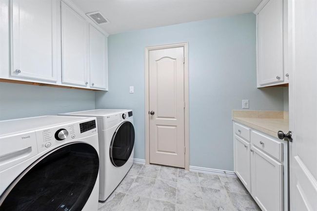 This bright and functional laundry room offers ample cabinet storage, tile flooring, and generous counter space for folding and organization. | Image 18