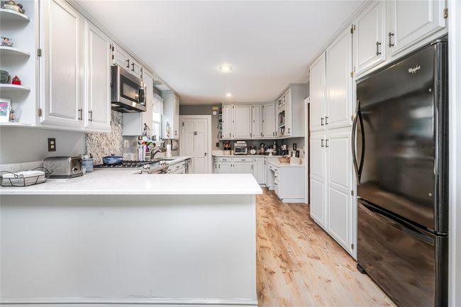 Kitchen featuring light countertops, stainless steel microwave, freestanding refrigerator, a peninsula, and light wood-style flooring | Image 13