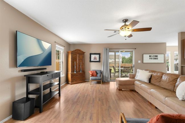 This inviting living area boasts a ceiling fan, elegant light wood flooring, and an abundance of natural light, creating a warm and welcoming atmosphere perfect for relaxation and entertainment. | Image 14