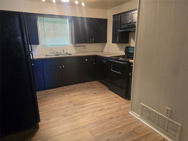 Kitchen featuring black appliances, under cabinet range hood, light wood finished floors, light countertops, and dark cabinetry | Image 6