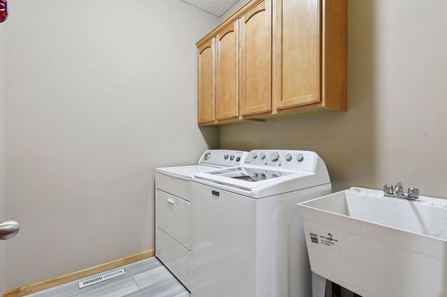 Main level laundry room features maple cabinetry, utility sink and brand new washing machine | Image 10