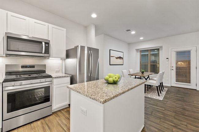 Kitchen featuring visible vents, decorative backsplash, stainless steel appliances, wood finished floors, and white cabinetry | Image 9