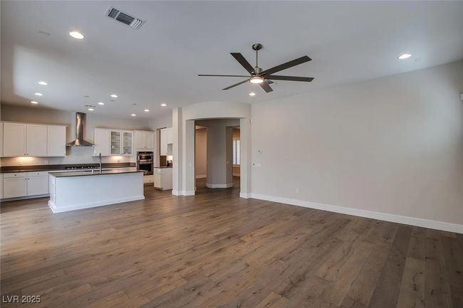 Kitchen with dark countertops, visible vents, open floor plan, wall chimney exhaust hood, and a ceiling fan | Image 4