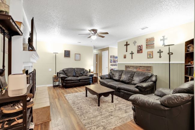 Living room with a fireplace, a ceiling fan, light wood-style floors, a textured ceiling, and crown molding | Image 13