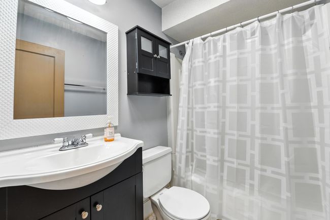 Updated full bath featuring modern vanity, framed mirror, over-toilet storage cabinet, and shower/tub combo with geometric curtain. | Image 23