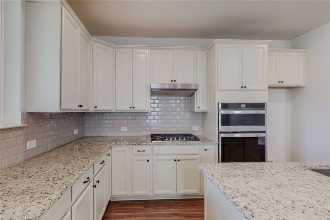 Kitchen featuring under cabinet range hood, stainless steel appliances, dark wood-type flooring, light stone counters, and decorative backsplash | Image 8