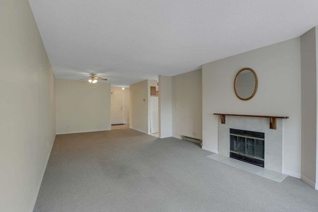 Unfurnished living room featuring a fireplace, light carpet, a baseboard radiator, and ceiling fan | Image 8