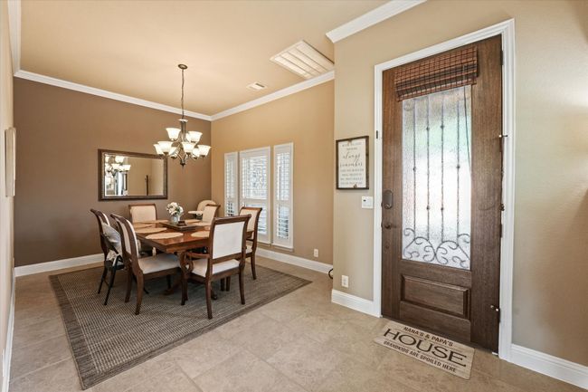 Dining space with crown molding, light tile patterned flooring, baseboards, a notable chandelier, and visible vents | Image 6
