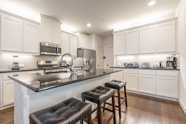 Kitchen with decorative backsplash, a kitchen breakfast bar, dark wood-style floors, and stainless steel appliances | Image 7