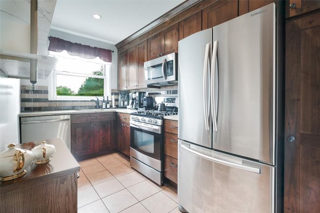 Kitchen featuring stainless steel appliances, a sink, light tile patterned floors, decorative backsplash, and light countertops | Image 5