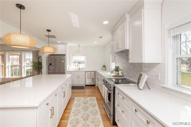 Kitchen with a kitchen island, light wood finished floors, stainless steel appliances, white cabinets, and decorative backsplash | Image 11