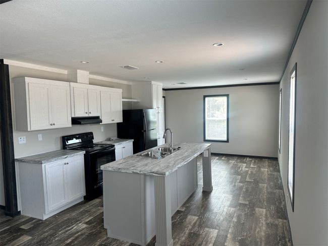 Kitchen featuring dark wood-style flooring, under cabinet range hood, a center island with sink, a sink, and black appliances | Image 6