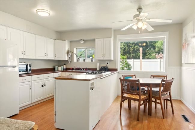 Kitchen featuring freestanding refrigerator, stainless steel microwave, light wood finished floors, white cabinets, and a ceiling fan | Image 7