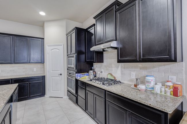 Kitchen featuring stainless steel appliances, under cabinet range hood, light tile patterned flooring, tasteful backsplash, and a warming drawer | Image 14