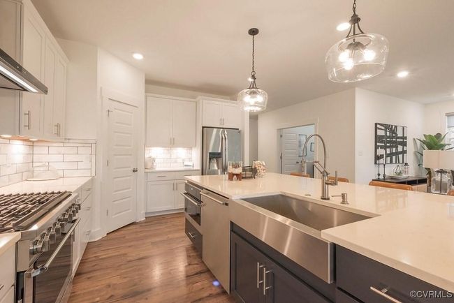 Kitchen with appliances with stainless steel finishes, white cabinetry, light countertops, backsplash, and hanging light fixtures | Image 31