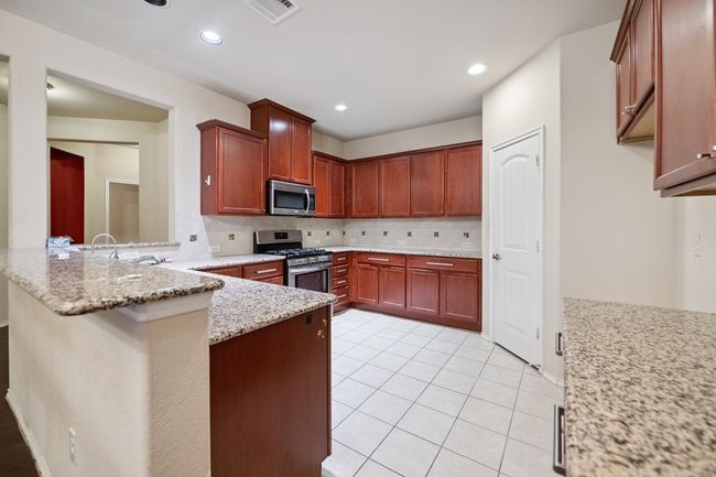 Kitchen featuring appliances with stainless steel finishes, backsplash, a peninsula, light stone counters, and light tile patterned floors | Image 5