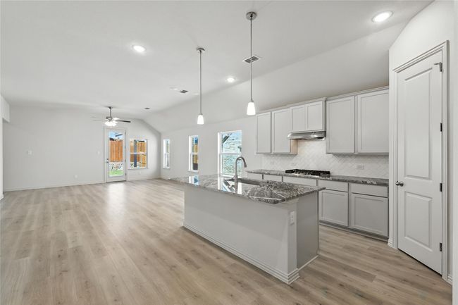 Kitchen with vaulted ceiling, stainless steel gas cooktop, under cabinet range hood, backsplash, and ceiling fan | Image 8