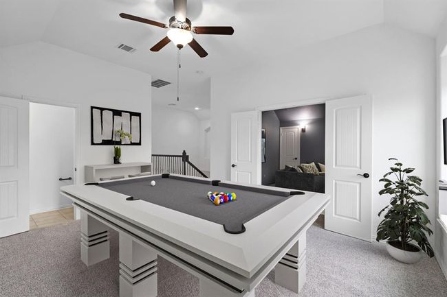 The spacious game room features cozy carpet, ample natural light from the windows, and a charming sloped ceiling, creating a perfect space for entertainment and relaxation. *Virtually Staged* | Image 13