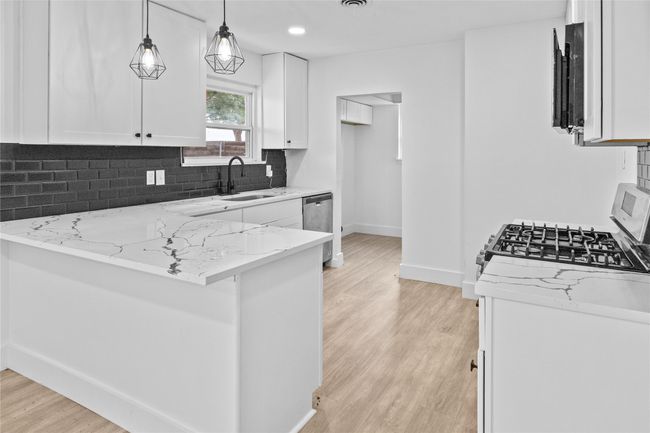 Kitchen with a sink, light stone countertops, a peninsula, baseboards, and white cabinets- Virtually staged | Image 7