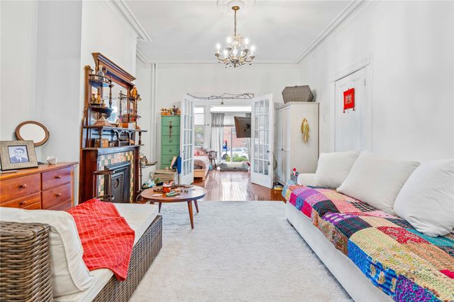 Bedroom with crown molding, a notable chandelier, a glass covered fireplace, french doors, and wood finished floors | Image 4