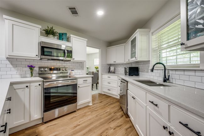 Kitchen with stainless steel appliances, a sink, tasteful backsplash, white cabinetry, and light countertops | Image 7