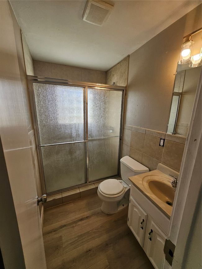 Bathroom with tile walls, wood finished floors, visible vents, and a stall shower | Image 7