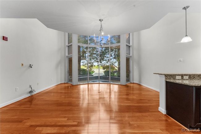 Unfurnished dining area featuring wood finished floors, floor to ceiling windows, a high ceiling, baseboards, and a notable chandelier | Image 13