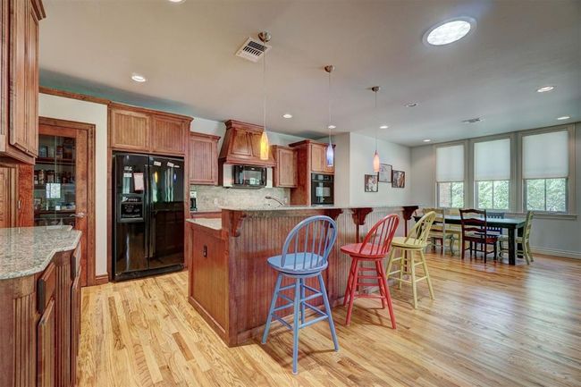 Kitchen with hanging light fixtures, black appliances, light wood-style floors, a breakfast bar area, and visible vents | Image 11