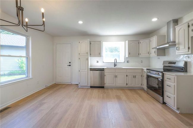 Kitchen featuring stainless steel appliances, wall chimney exhaust hood, light countertops, a chandelier, and light wood-style floors | Image 6
