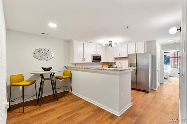 Kitchen with stainless steel appliances, light wood-style flooring, white cabinets, and backsplash | Image 4