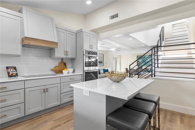 The kitchen is fully-equipped with built-in double ovens, a built-in microwave, dishwasher, and electric cooktop with a wood vent hood. | Image 15