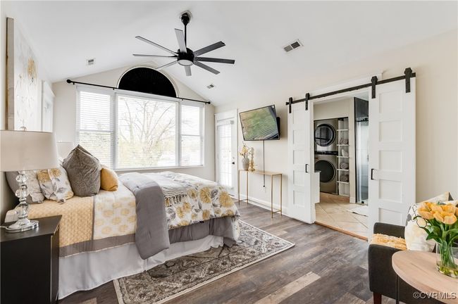 Bedroom with stacked washer and dryer, a barn door, wood finished floors, lofted ceiling, and visible vents | Image 34