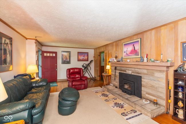 living area featuring wood finished floors, ornamental molding, a wood stove, wooden walls, and a textured ceiling | Image 6