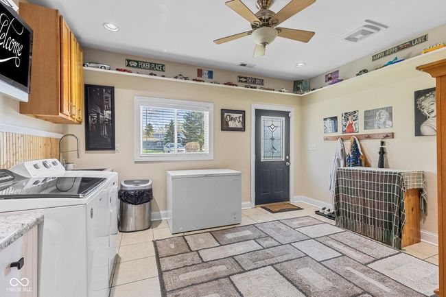 Large laundry area with ceiling fan, light tile patterned floors, and lots of cabinet space with door to the outside. | Image 20
