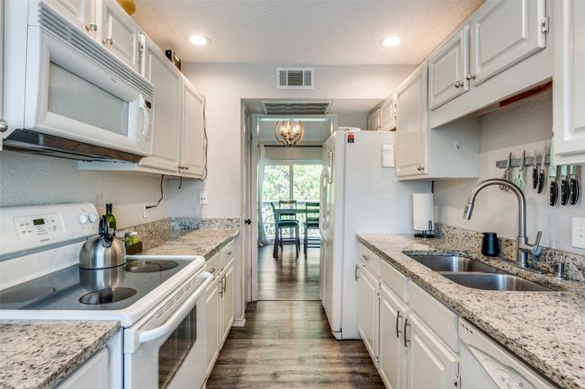 Kitchen featuring white appliances, a sink, wood finished floors, white cabinets, and a chandelier | Image 9