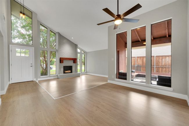 Unfurnished living room with high vaulted ceiling, a fireplace, a ceiling fan, and wood finished floors | Image 7