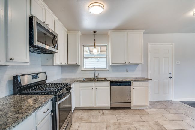Kitchen with a sink, white cabinetry, dark stone counters, stainless steel appliances, and decorative backsplash | Image 14