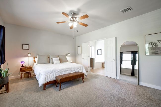 The 1st level primary suite is spacious and boasts a ceiling fan, carpet flooring, and a French door entry leading to the en-suite bathroom. | Image 16